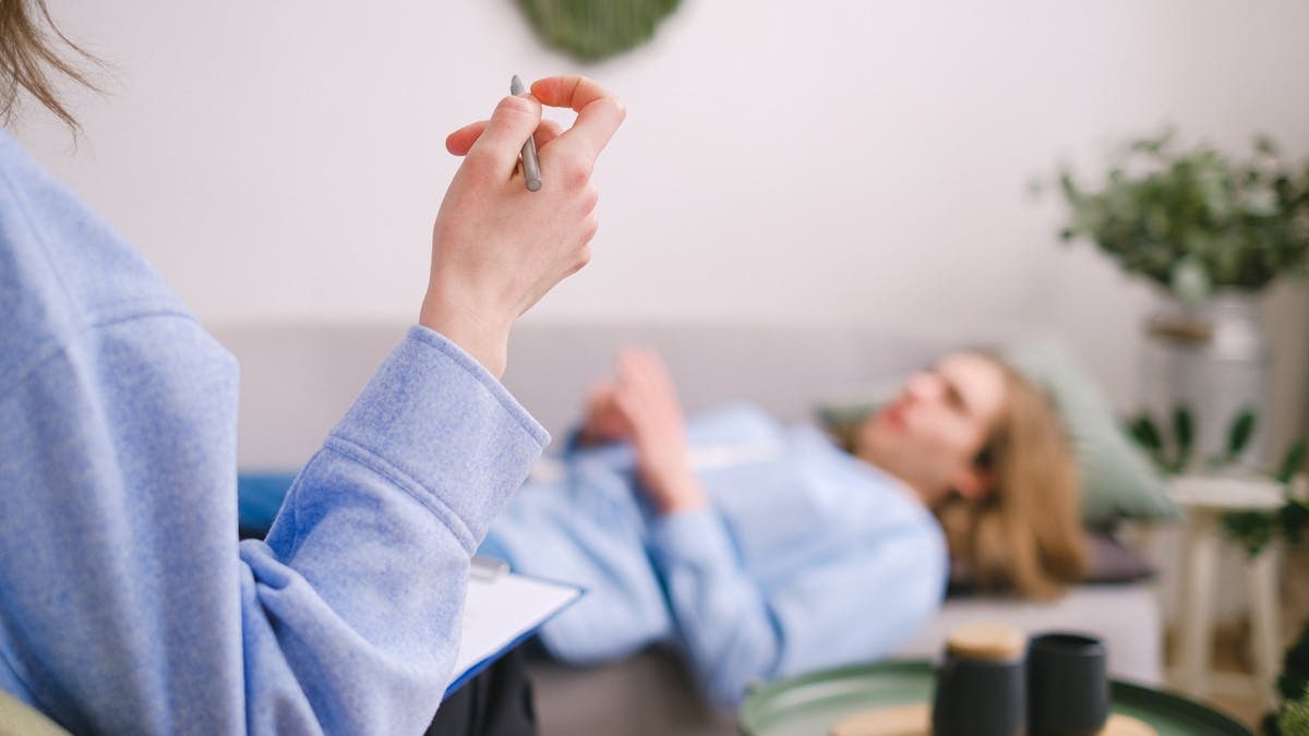 Therapist taking notes during a therapy session with a relaxed client lying on a couch.